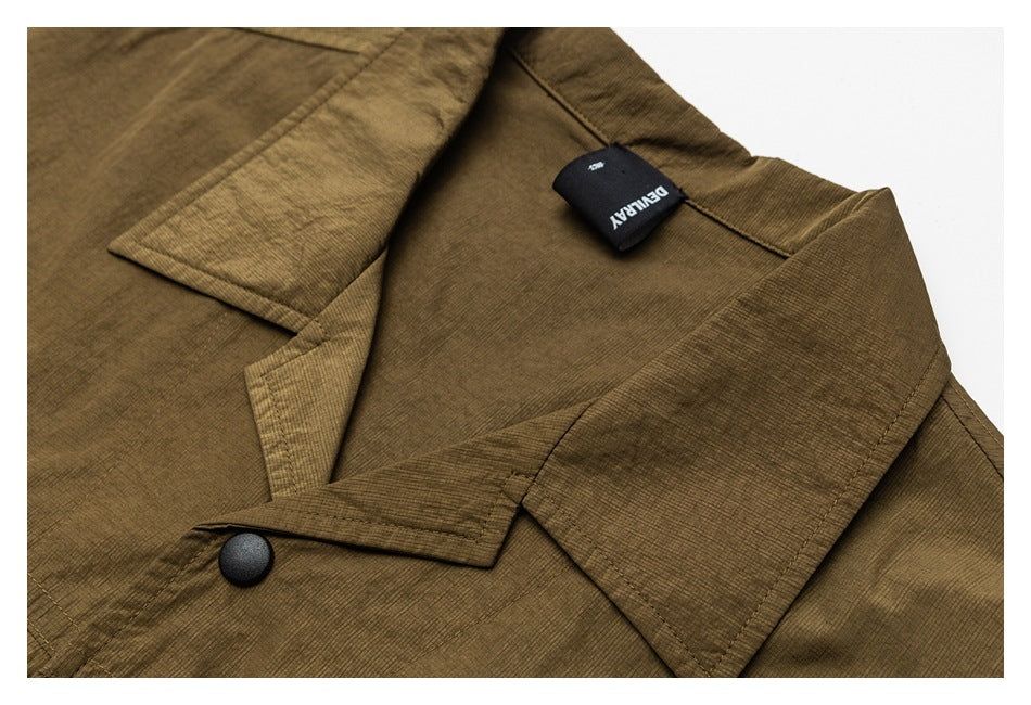 Close-up of an olive-brown jacket collar, lapel, black snap button, and attached black brand tag.