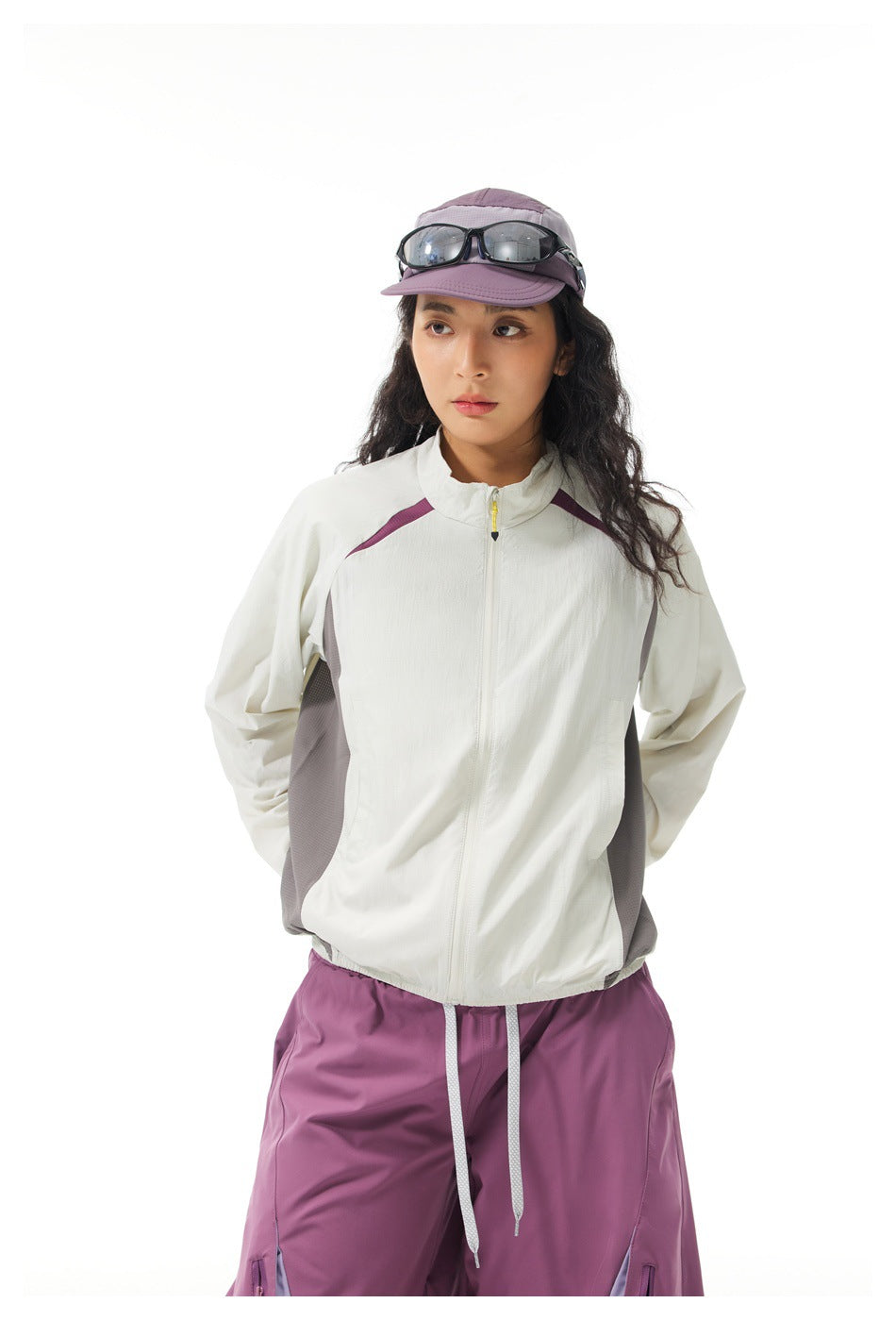 Model wearing an off-white zip jacket with gray side panels and plum pants, shown from the front.