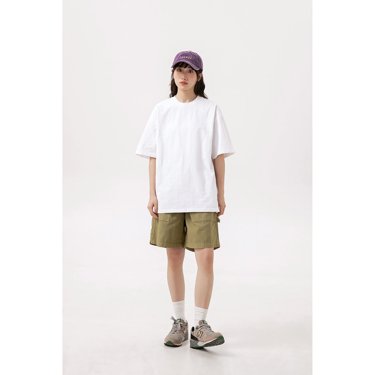 Model wearing an oversized white short-sleeve T-shirt with olive cargo shorts and a purple cap.