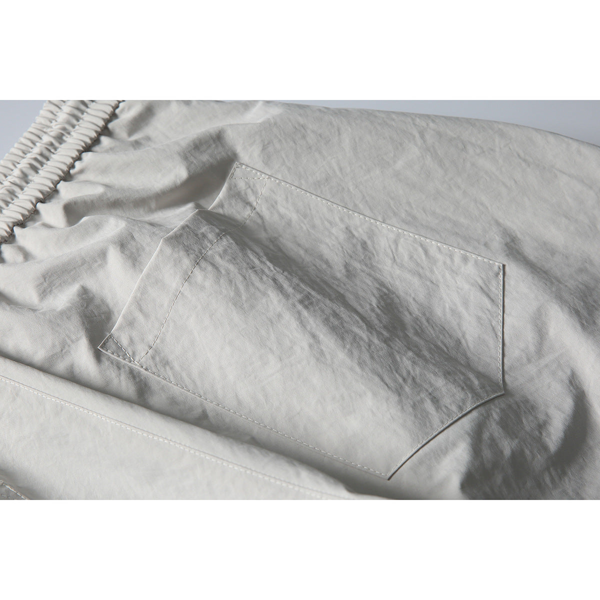 Close-up of light gray pants showing a large stitched rear patch pocket and part of the elastic waistband.
