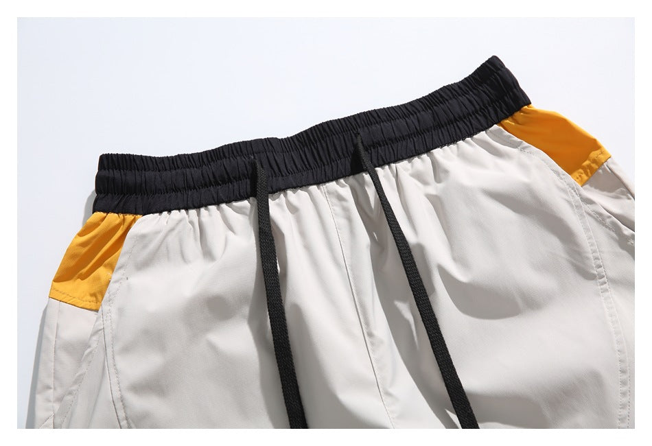 Close-up of light gray shorts with a black elastic drawstring waistband and mustard-yellow side panels.