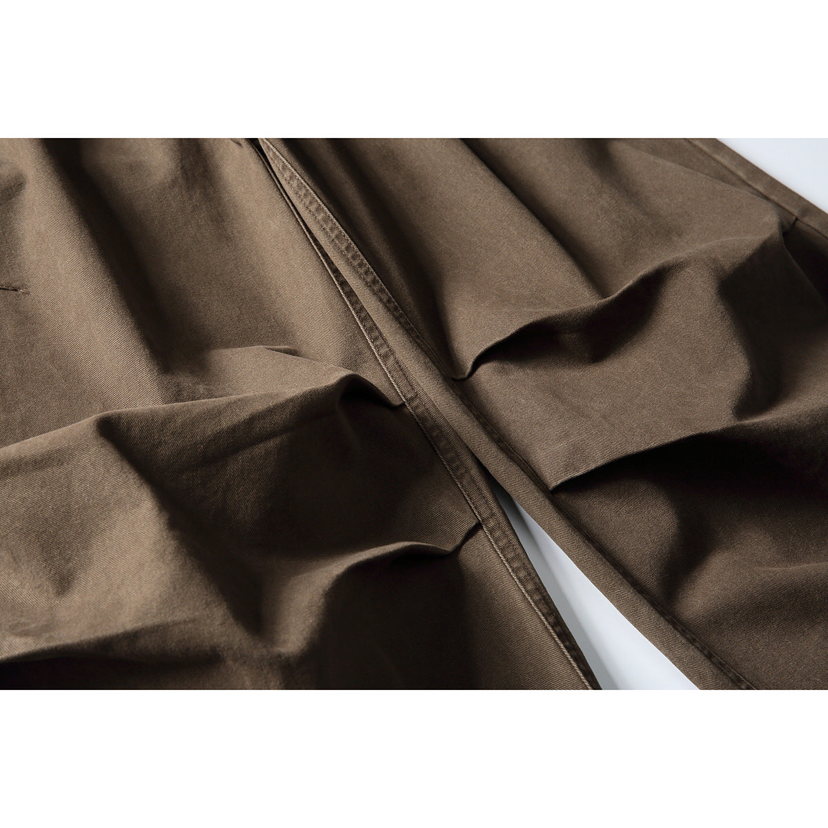 Close-up of brown trousers highlighting the front seam and folded fabric.