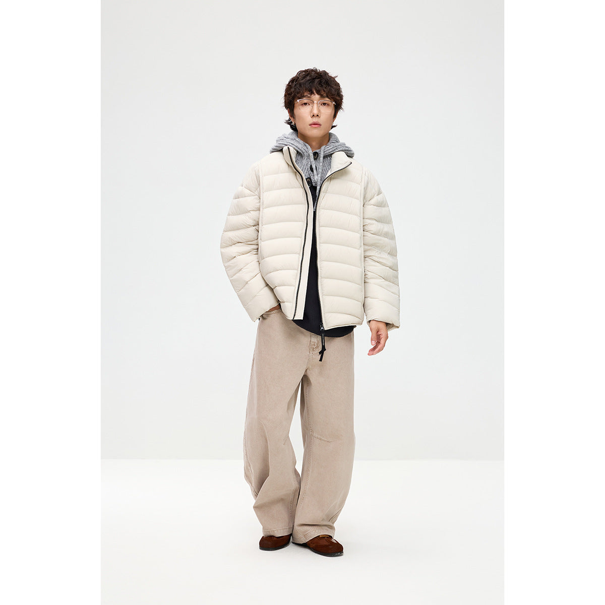 Model wearing an off-white quilted puffer jacket over a gray hooded top and loose beige trousers.