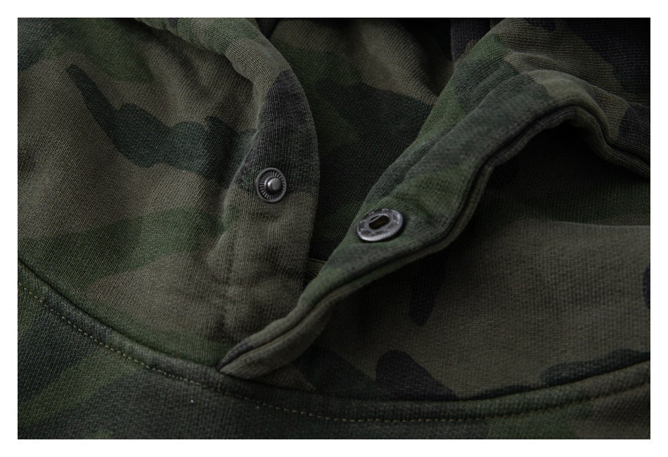 Close-up of dark green camouflage fabric showing two metal snap fasteners and a stitched edge.