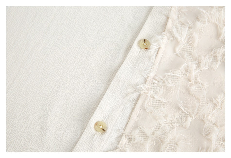 Close-up of two cream buttons along the white shirt placket beside frayed floral appliqué.