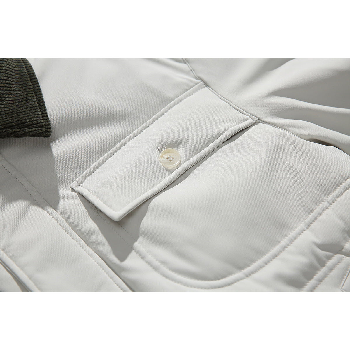 Close-up of the off-white jacket's buttoned chest pocket, curved lower pocket and dark ribbed collar edge.