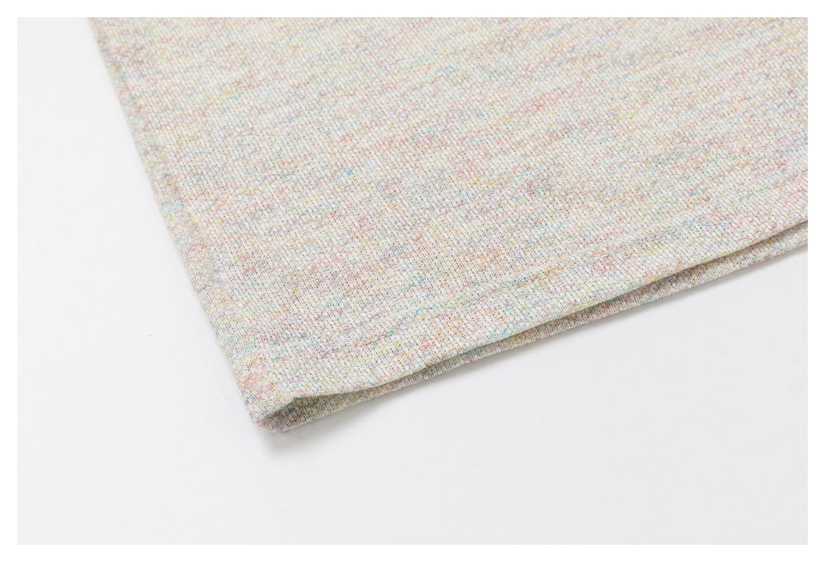Close-up of a folded hem on pale, multicolored-speckled fabric.