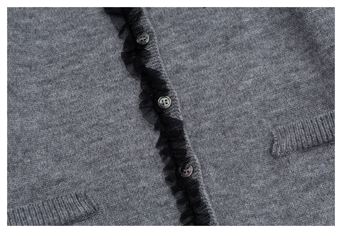 Close-up of a gray knit cardigan’s black ruffled button placket, decorative buttons, and ribbed pocket edges.