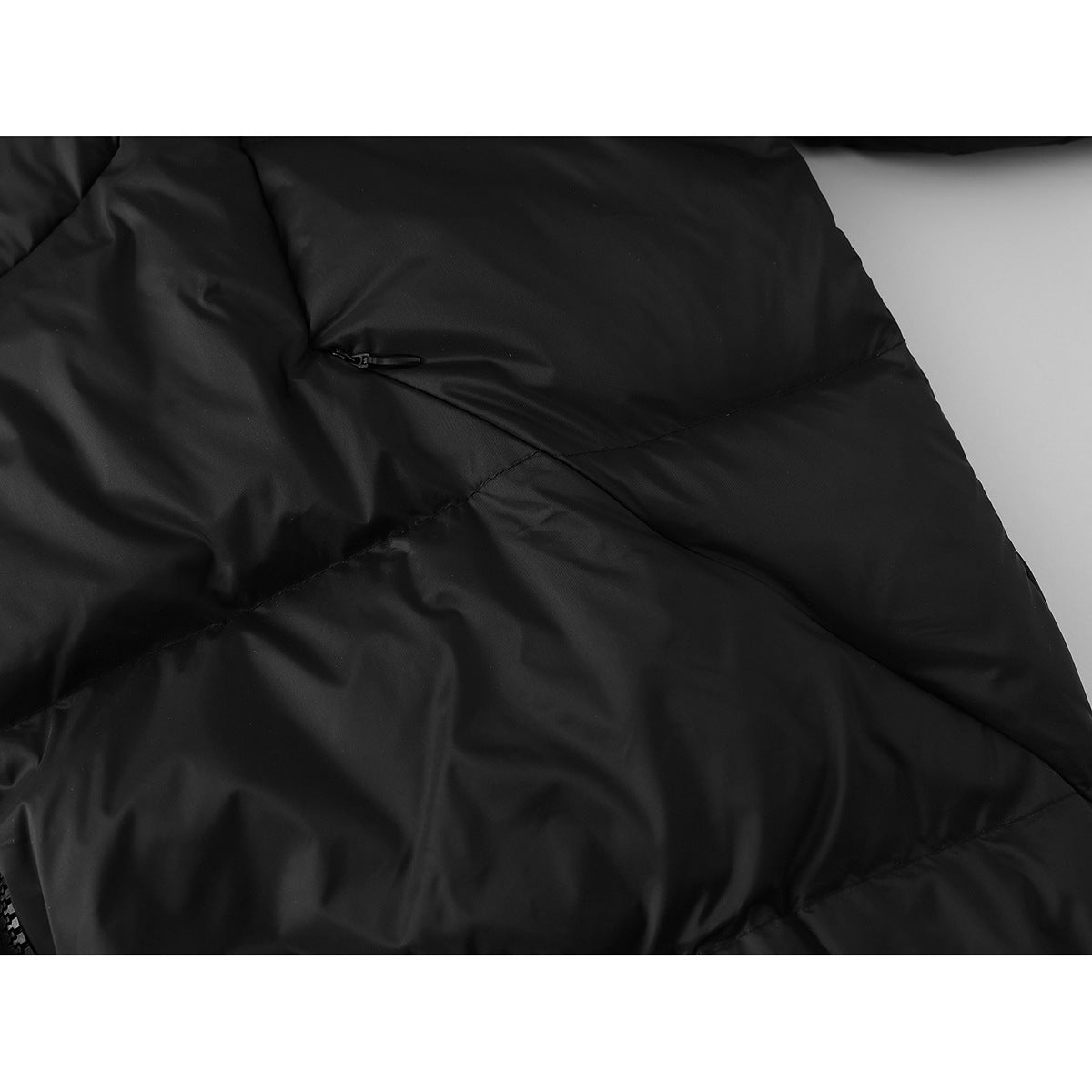 Close-up of black quilted jacket fabric with a small zip pocket and diagonal seam.