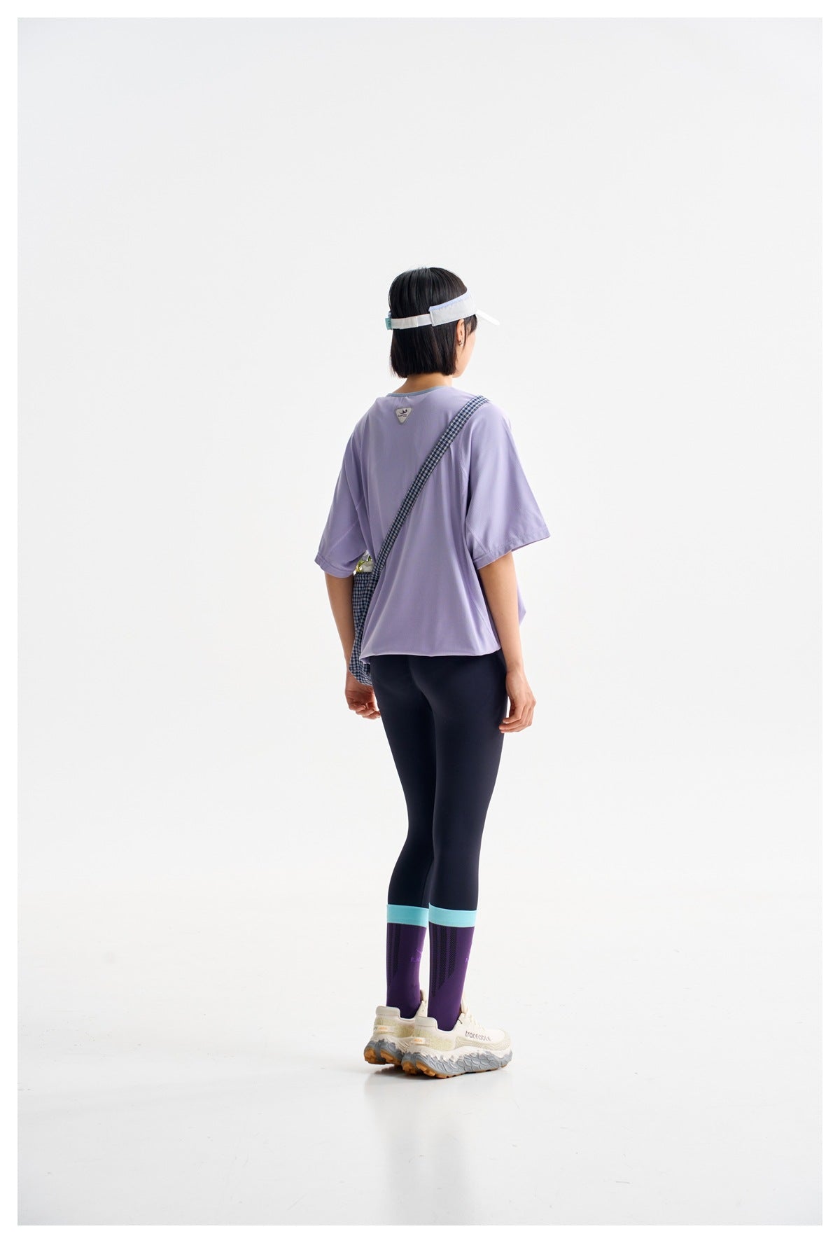 Back view of a model in a loose lavender tee, dark leggings and purple socks with turquoise bands.
