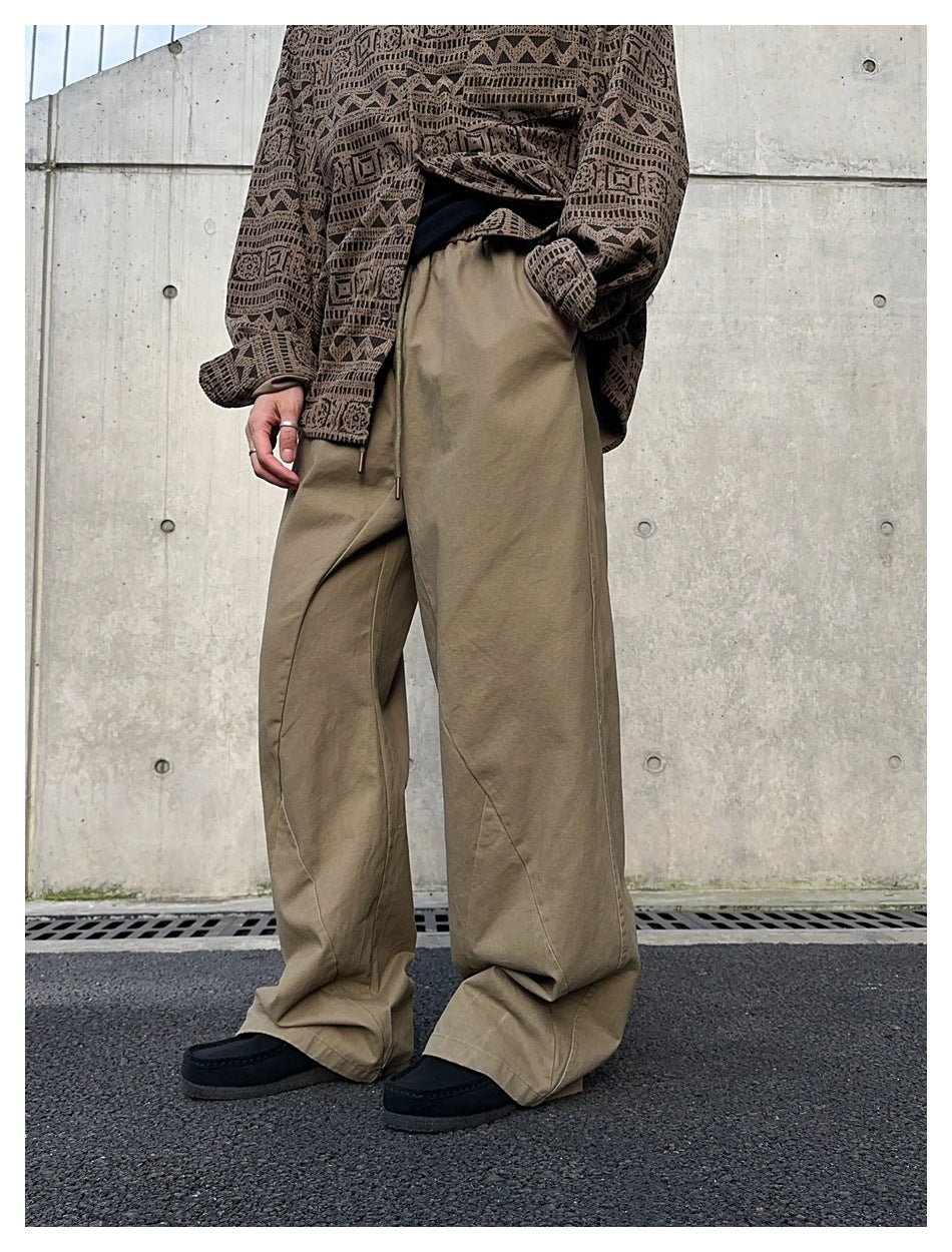 Closer angled view of taupe wide-leg drawstring pants worn with a patterned brown shirt.