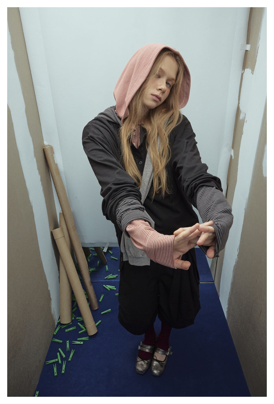 Model wearing a black hooded top with red-and-white striped hood and cuffs, gray layer, and black bottoms.
