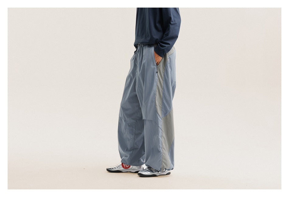 Side view of a model wearing loose blue-gray pants with contrasting pale side panels and gathered hems.