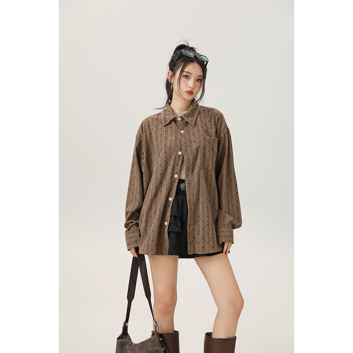 Model wearing an oversized brown patterned button-up shirt with a chest pocket and black shorts, front view.