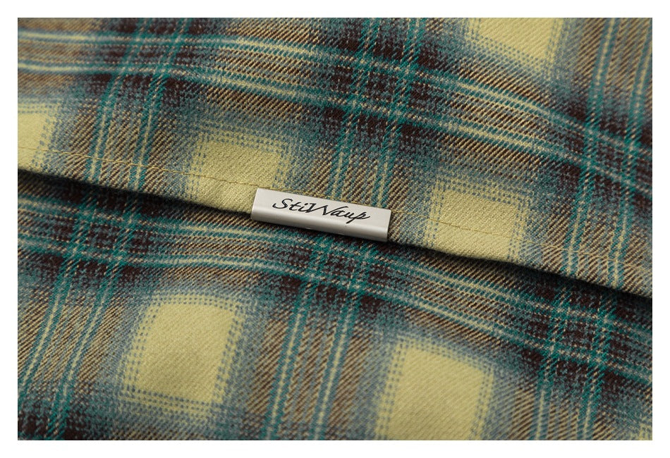 Close-up of a small sewn brand label on tan, teal, and brown plaid fabric.