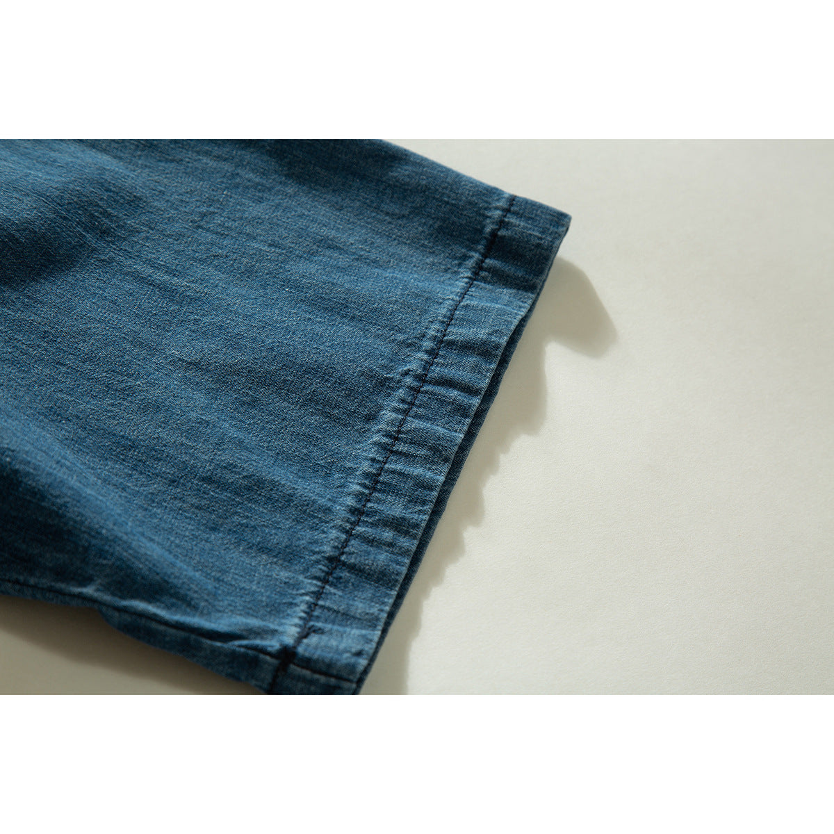 Close-up of the stitched hem on a blue denim shirt sleeve.