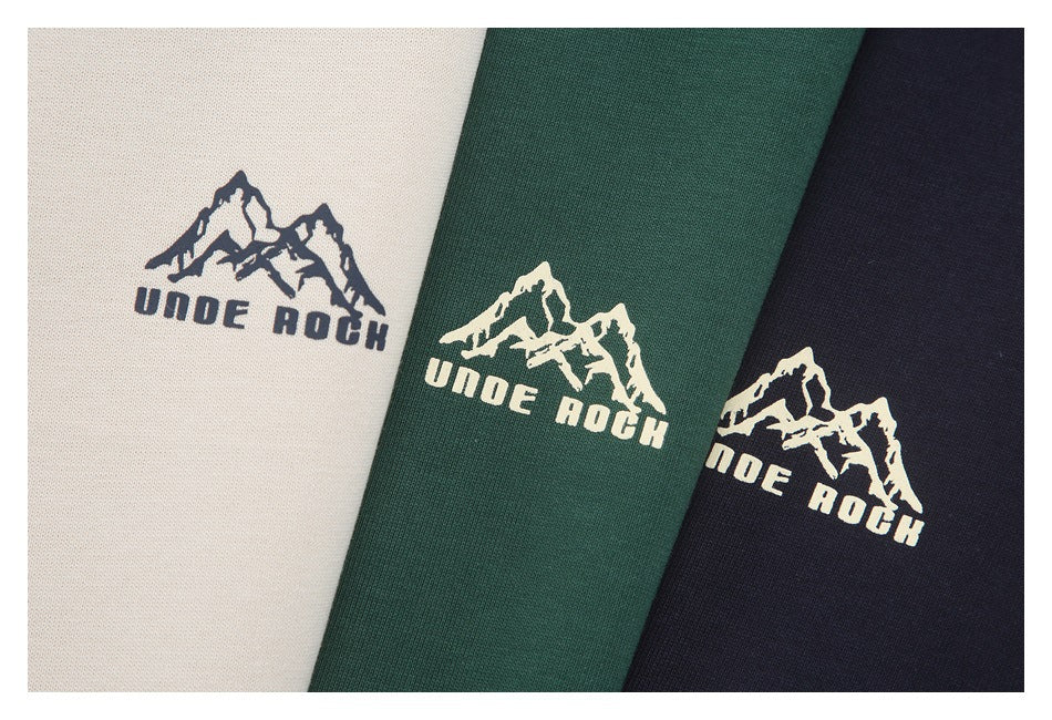 Close-up of three shirts in beige, forest green, and navy, each with a mountain logo print.