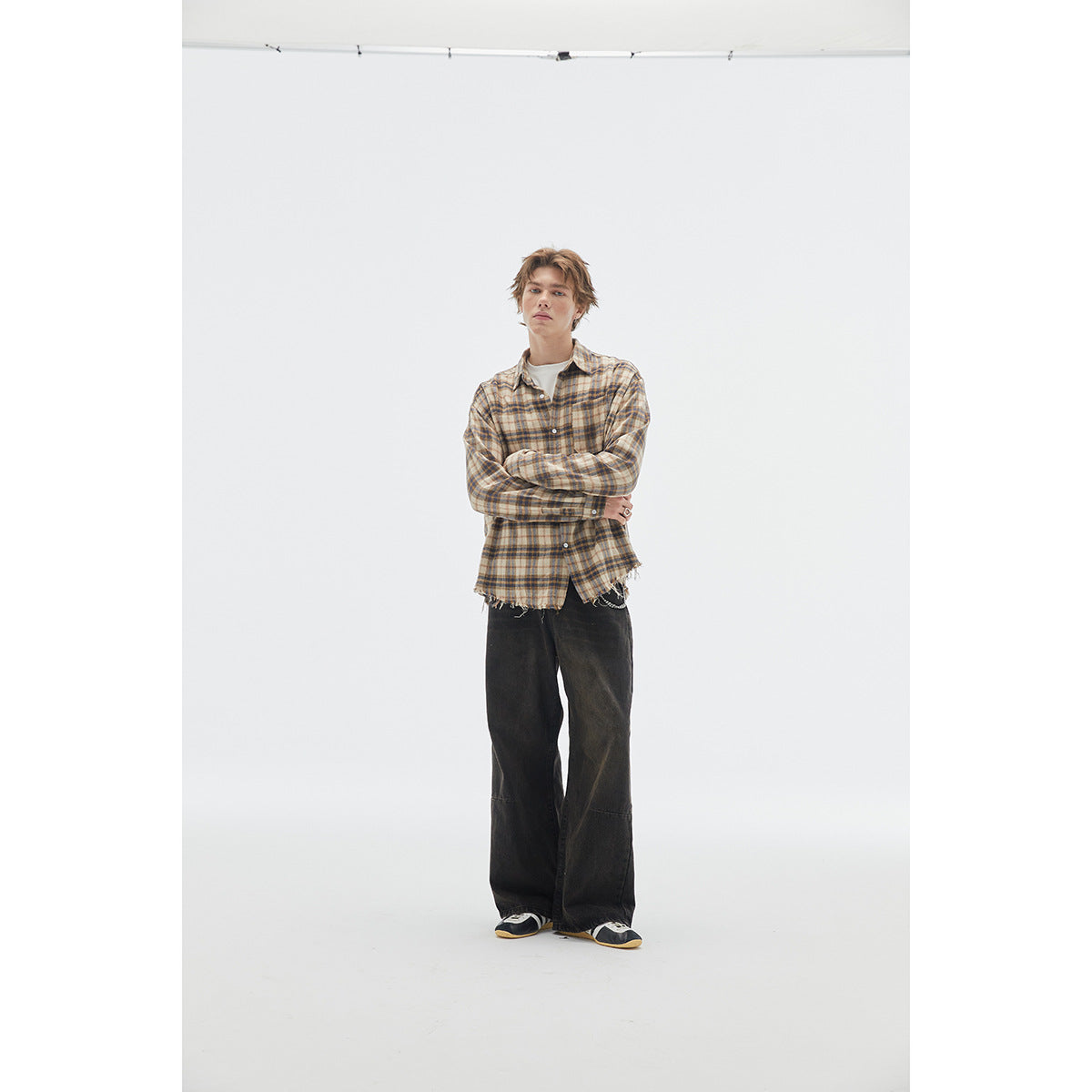 Model wearing a beige and blue plaid shirt with a frayed hem, black wide-leg trousers and sneakers.