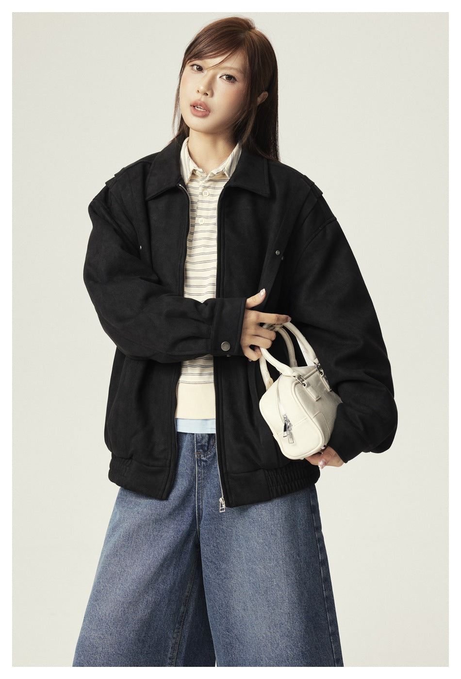Model wearing a black suede-look zip jacket over a striped polo with wide-leg jeans and a white handbag