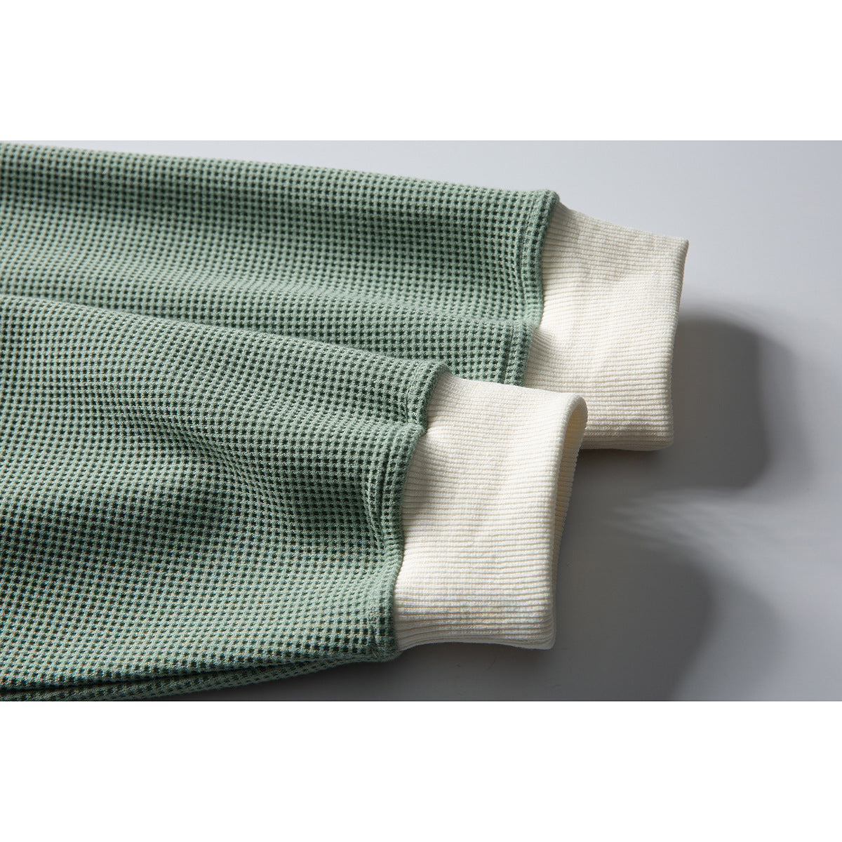 Close-up of sage-green textured sweatshirt sleeves with contrasting ivory ribbed cuffs.