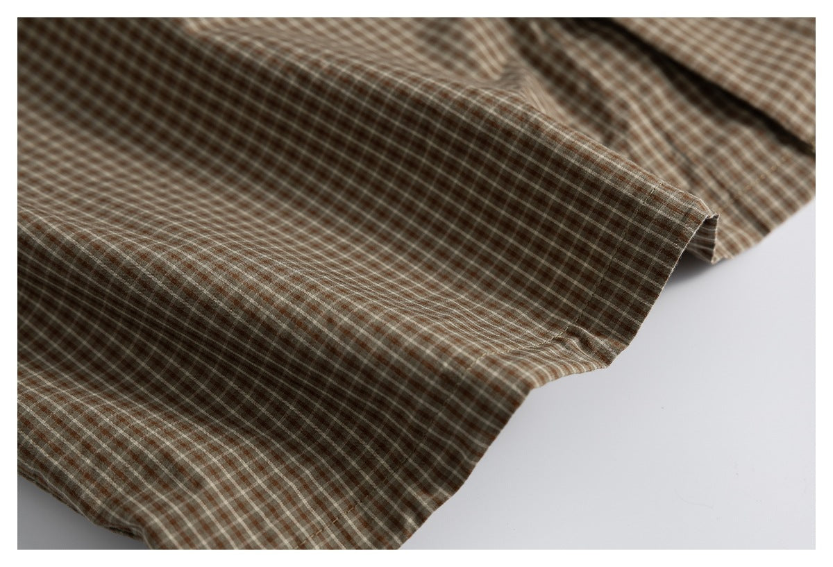 Close-up of the stitched hem and draped edge of a brown and cream checked shirt.