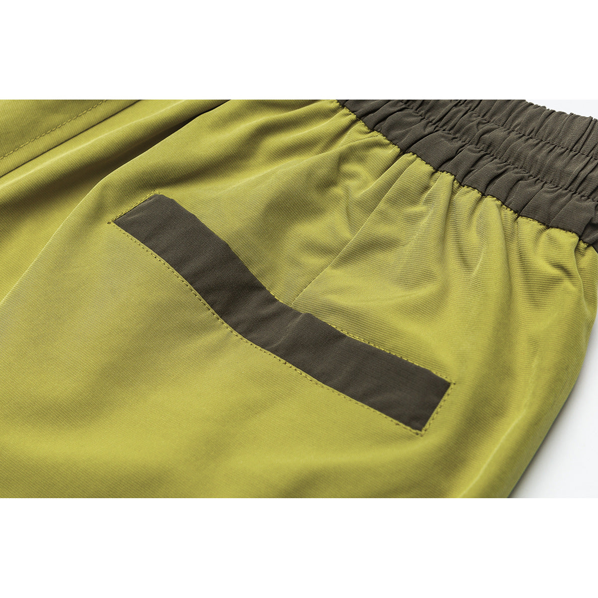 Close-up of a curved dark olive pocket detail on chartreuse shorts, with the elastic waistband visible.