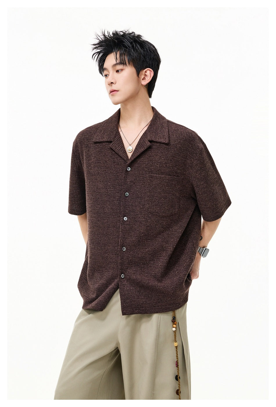 Model wearing a brown short-sleeve button-up shirt with a notched collar and chest pocket, shown from the front.