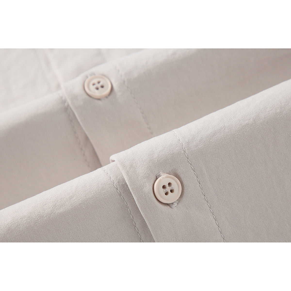 Close-up of off-white shirt fabric, stitching, and two four-hole buttons.