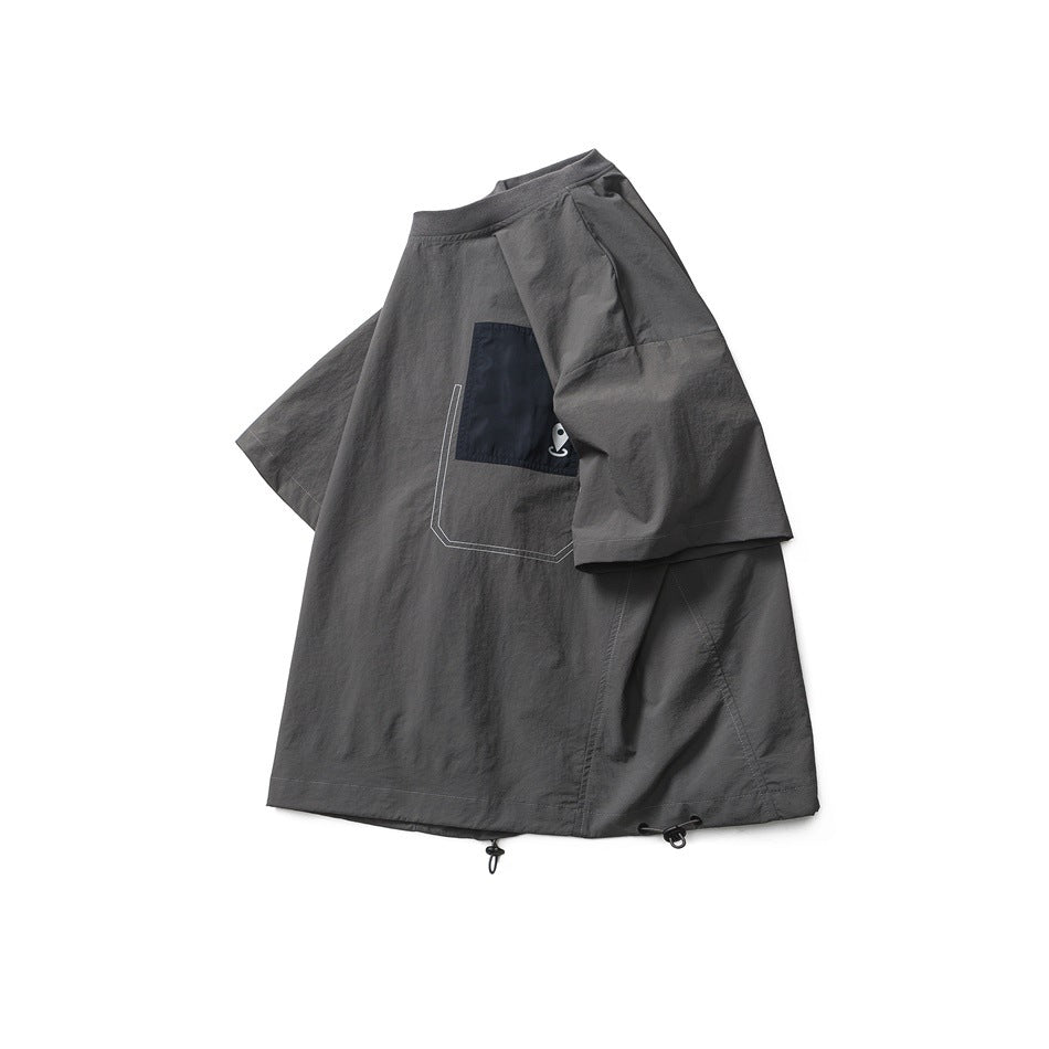 Gray T-shirt laid at an angle showing black chest pocket, sleeve seams and drawcord hem toggles