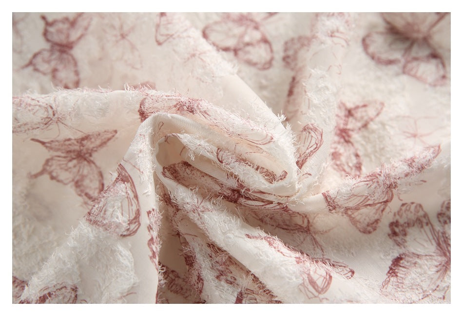 Close-up of draped ivory fabric with raised white texture and dusty rose butterfly print.