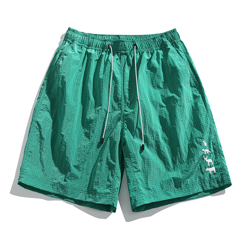 Jade green textured drawstring shorts with grid pattern and white animal embroidery near the hem, flat lay