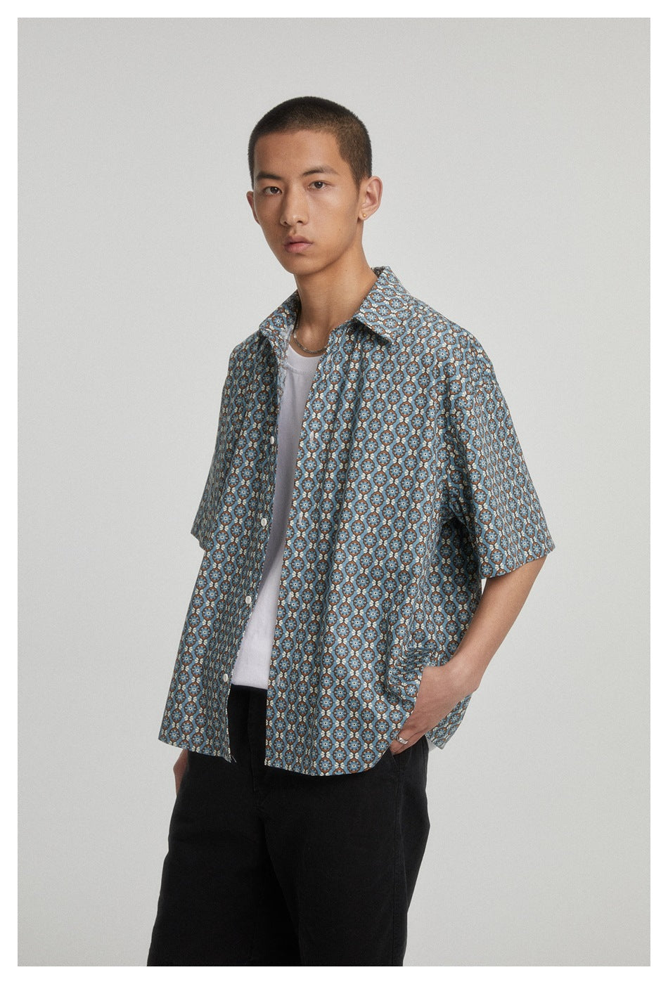 Closer view of a model wearing an open blue floral-patterned short-sleeve shirt over a white tee.