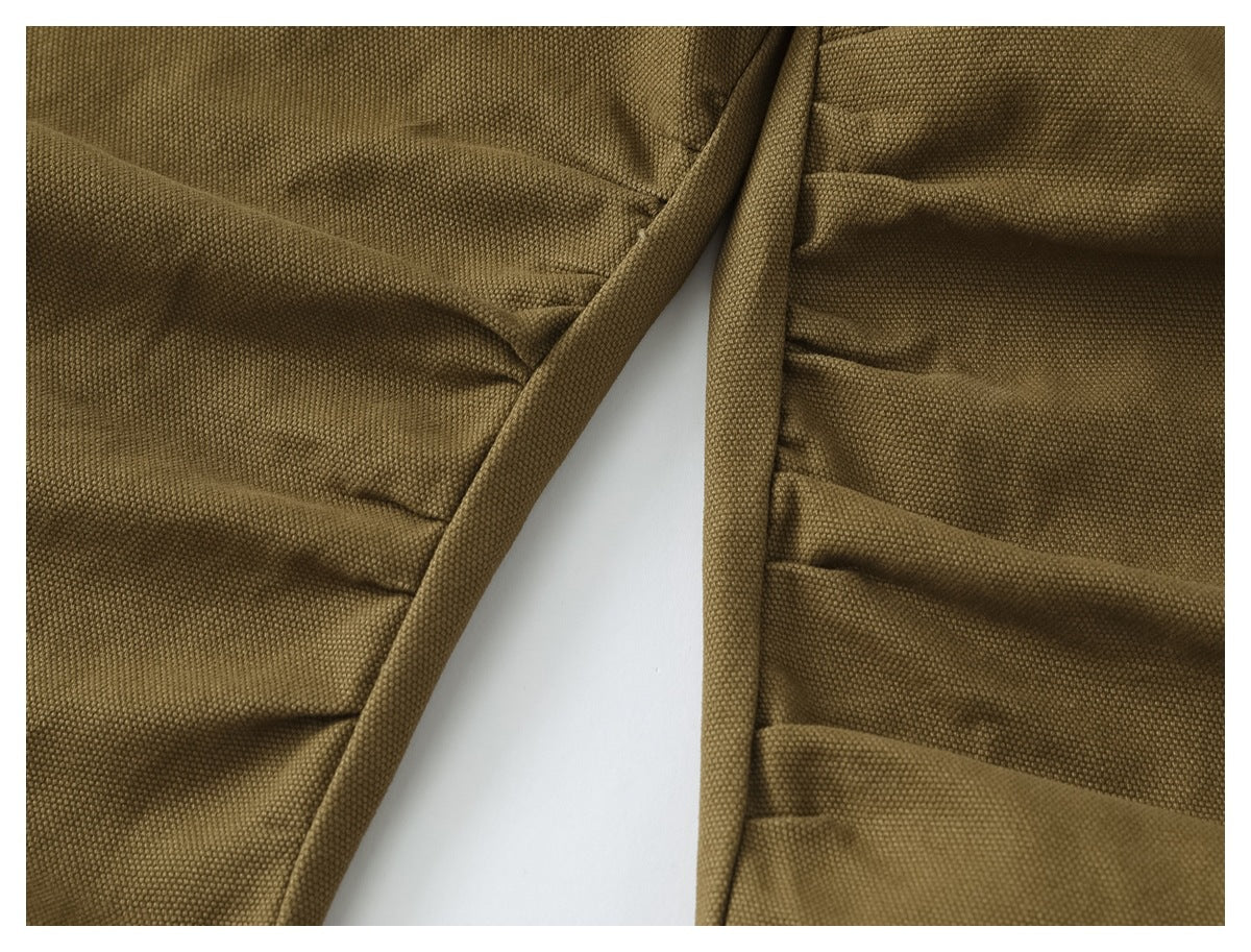 Close-up of olive-brown trouser fabric showing stitched seams and layered pocket construction.