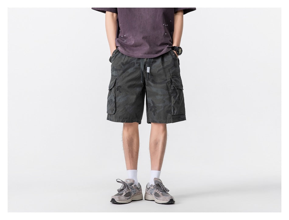 Front view of a model wearing dark charcoal camouflage cargo shorts with a drawstring waist and large side pockets.