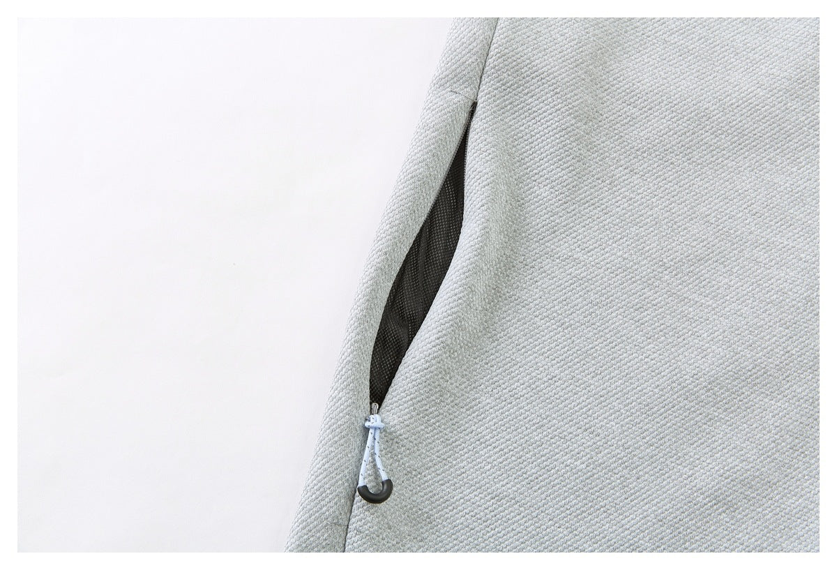 Close-up of a pale gray textured garment with a dark zippered opening and looped zipper pull.