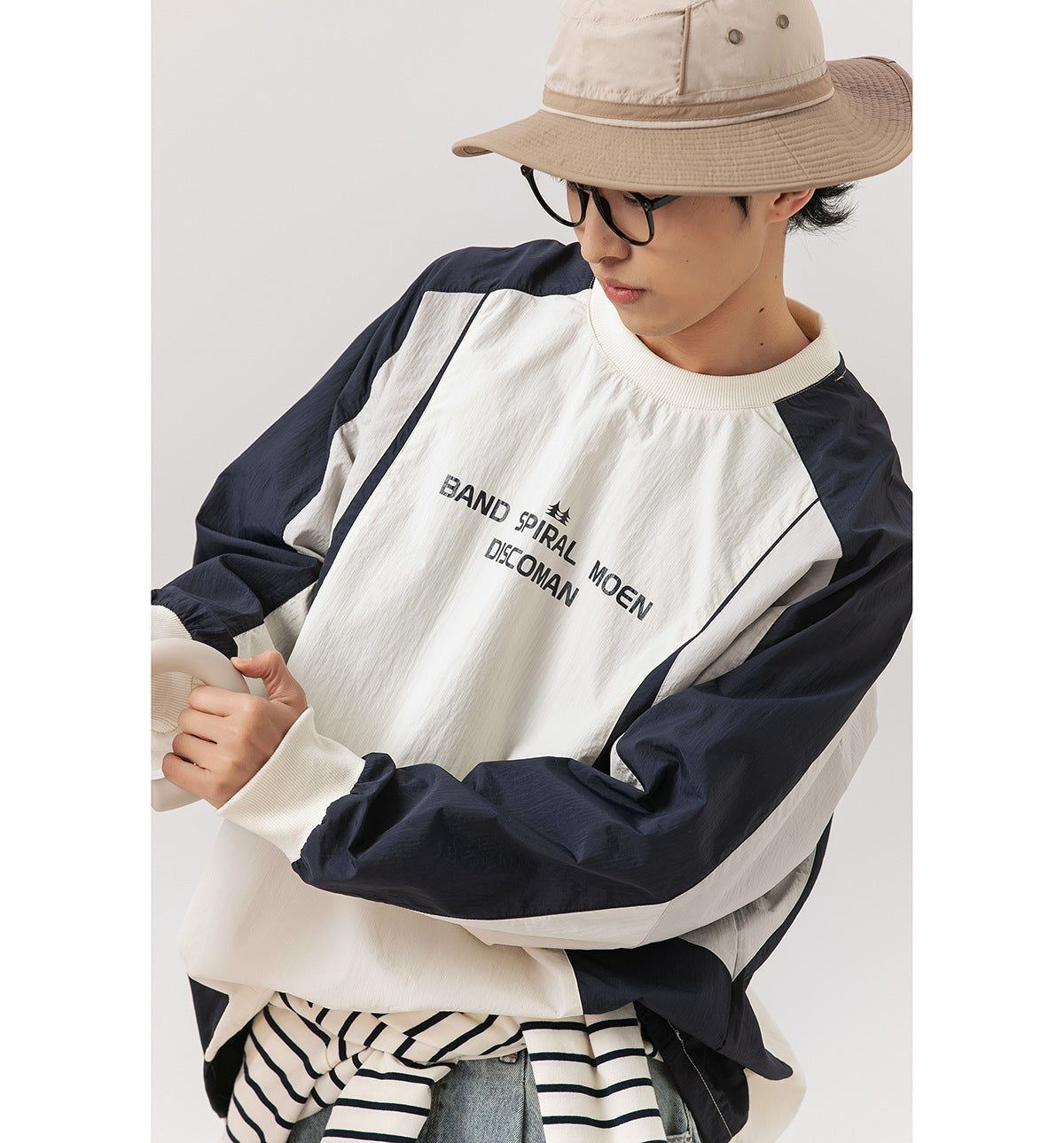 Close-up of a model wearing an ivory and navy color-block pullover with printed chest lettering and ribbed cuffs.