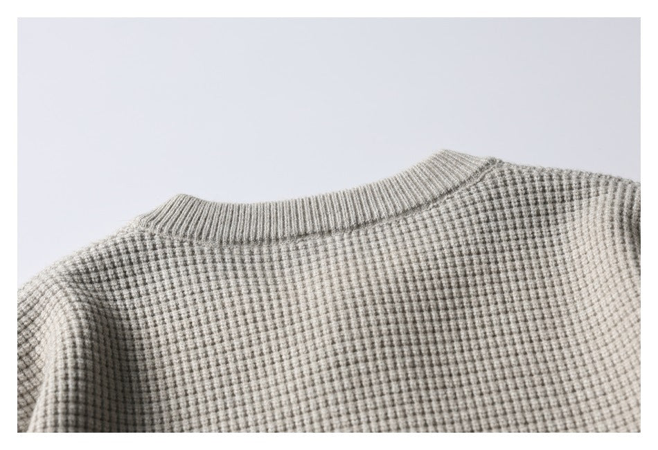 Close-up of the light gray textured knit garment's ribbed crew neckline and shoulders.