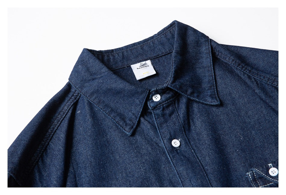 Close-up of a dark indigo shirt front showing the collar, white buttons and a partial chest pocket.