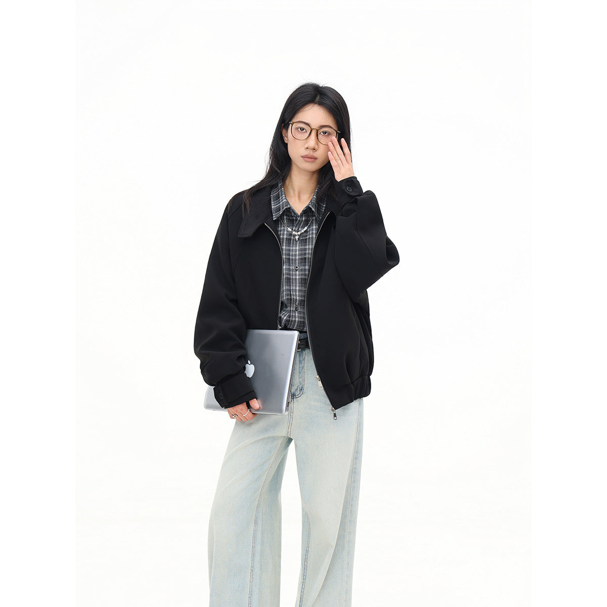 Model wearing an open black zip-front jacket over a gray plaid shirt and pale wide-leg jeans.