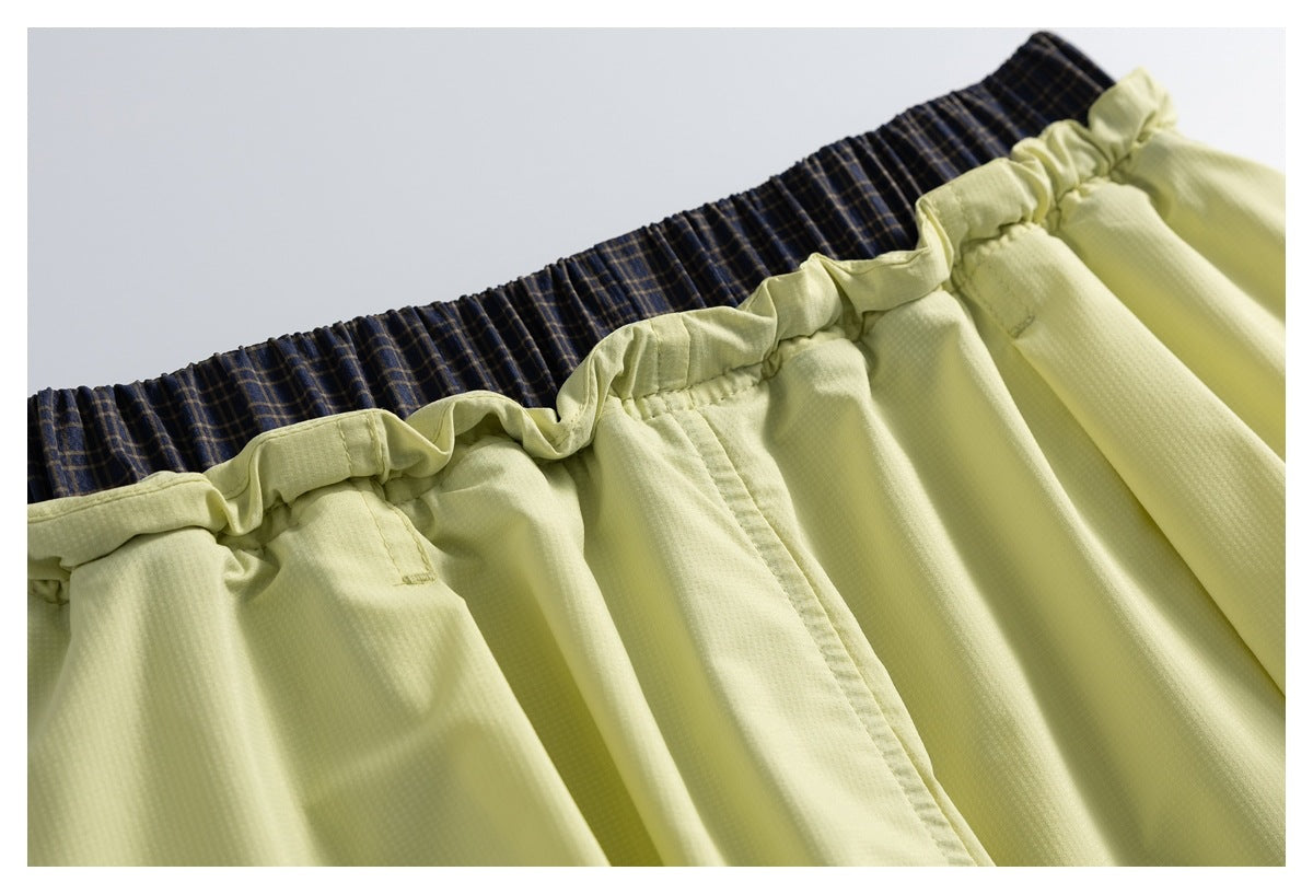 Close-up of a pale yellow garment's gathered waistband with dark plaid elastic inside.