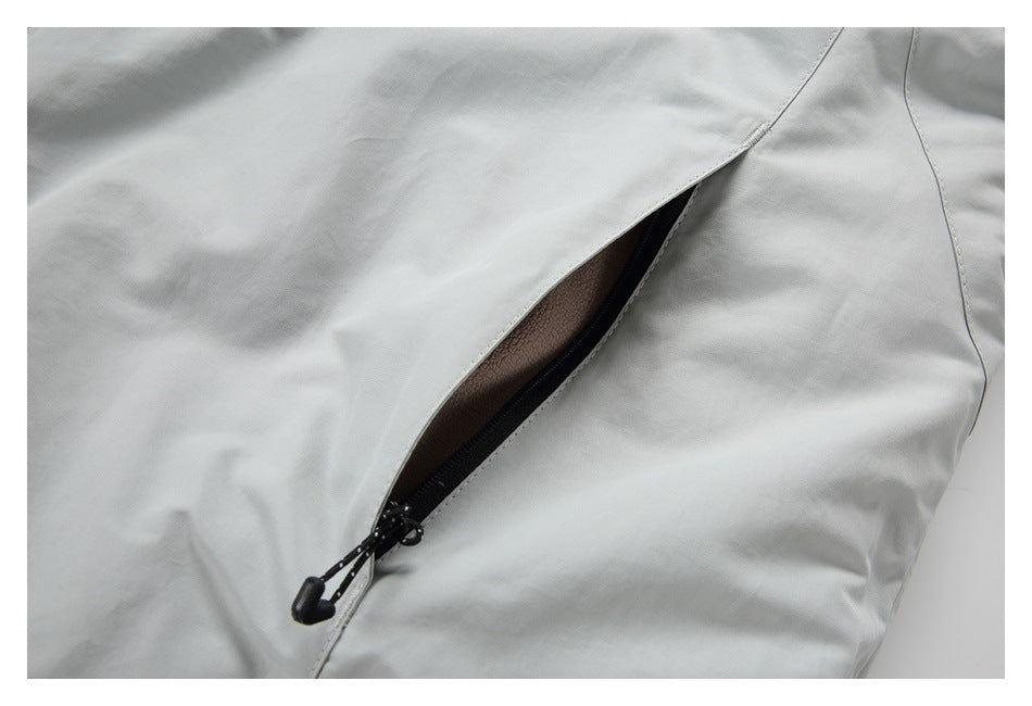 Close-up of a black zippered pocket with a pull tab on a light gray garment.