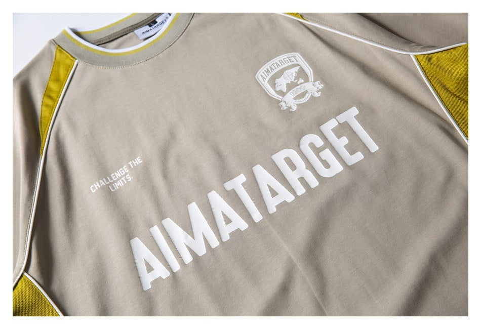 Close-up of the beige shirt front, showing a large white logo, crest, and yellow side panels.