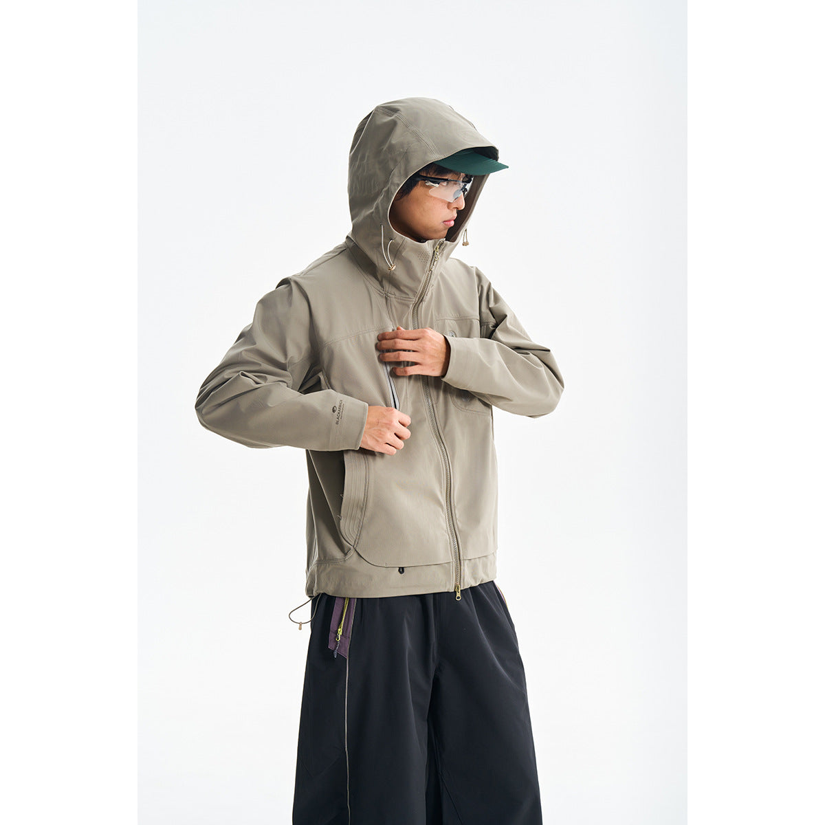 Model wearing a taupe hooded zip jacket with front pockets, shown against a white background.