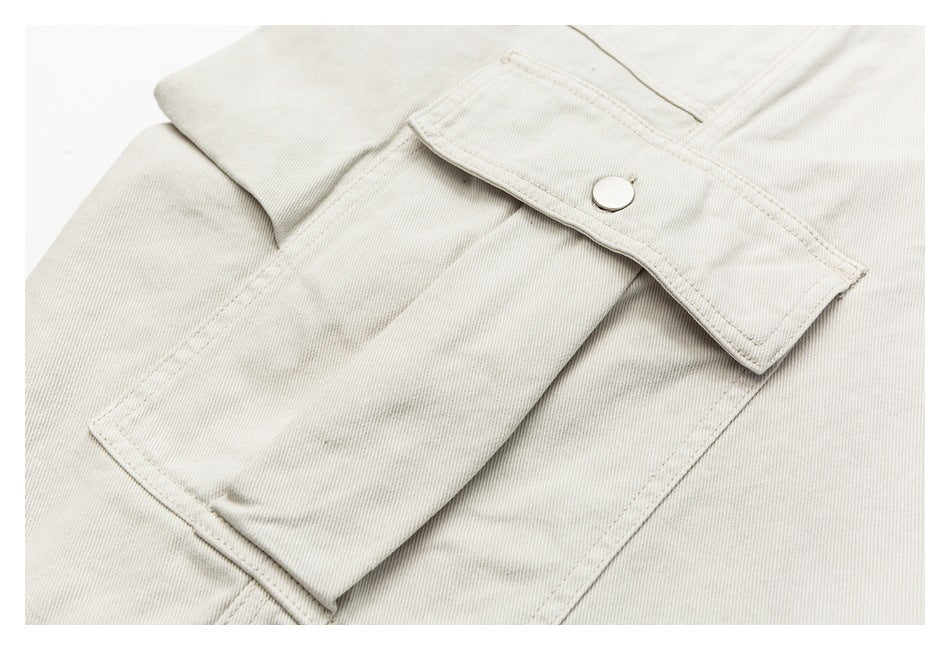 Close-up of an off-white garment showing a stitched flap pocket with a silver snap button.