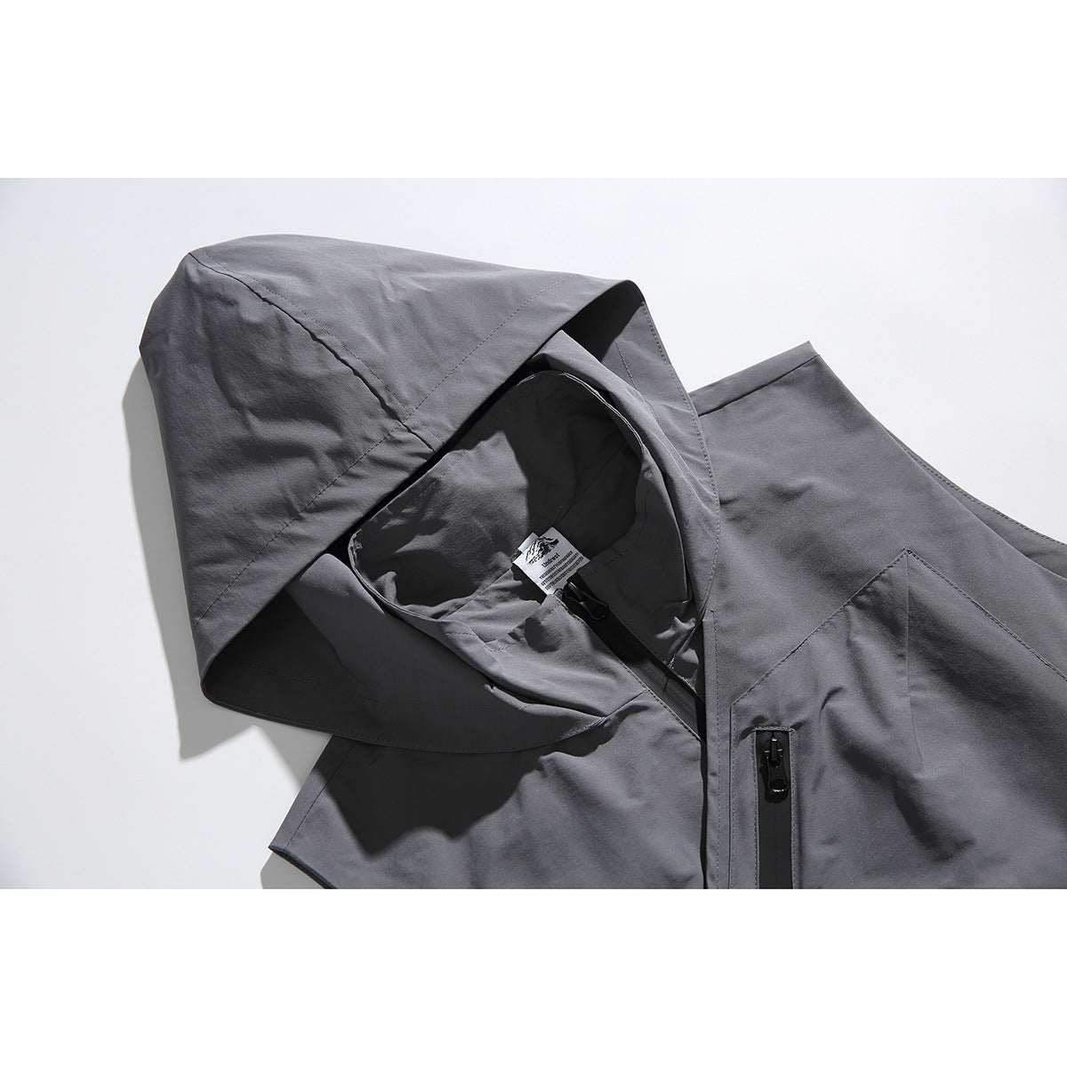 Close-up of a gray hooded vest showing the hood, inner label, and black front zipper.