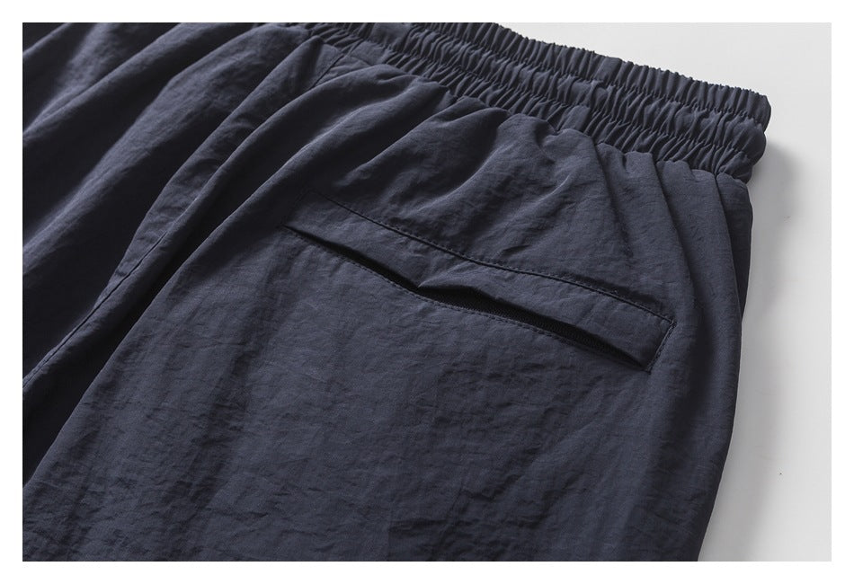 Close-up of dark navy pants showing the gathered elastic waistband and a slanted zip pocket.