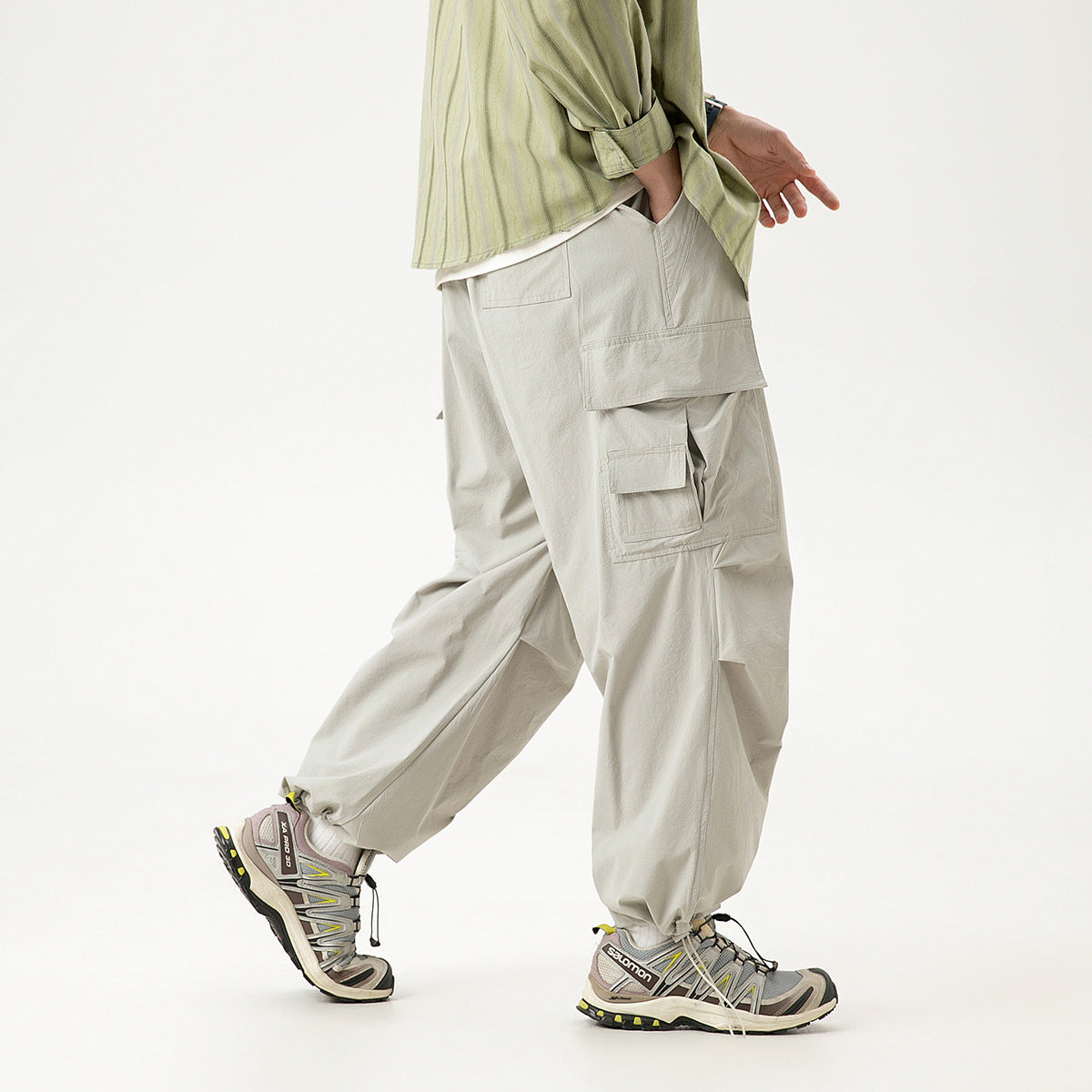 Model wearing loose light gray cargo pants with multiple pockets and gathered ankle cuffs, shown from the side.