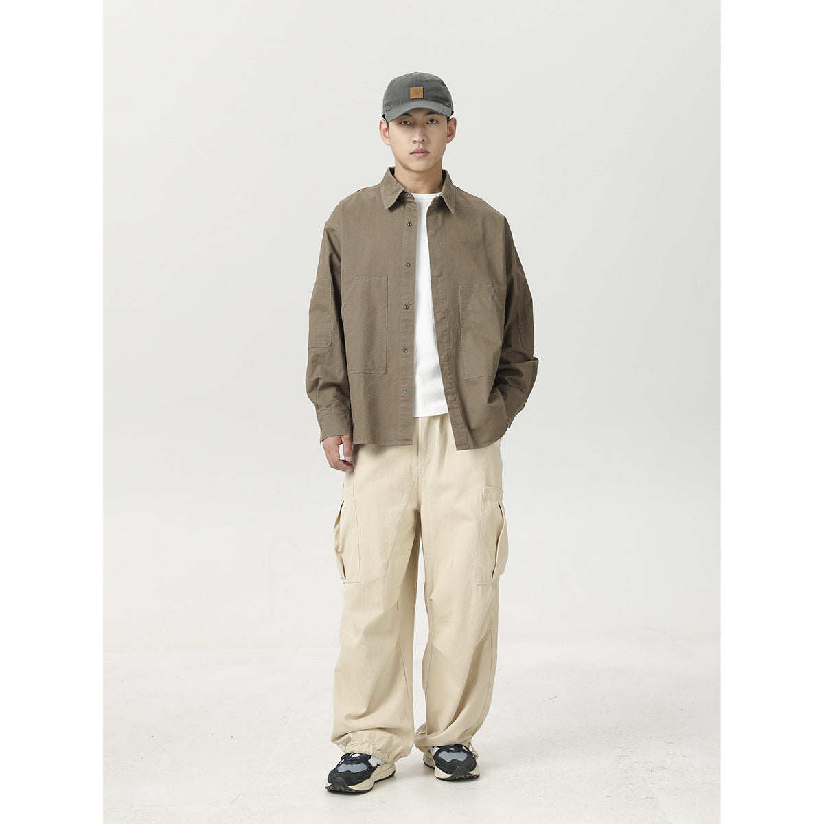 Model wearing a taupe button-front shirt, white tee, and loose cream cargo pants.