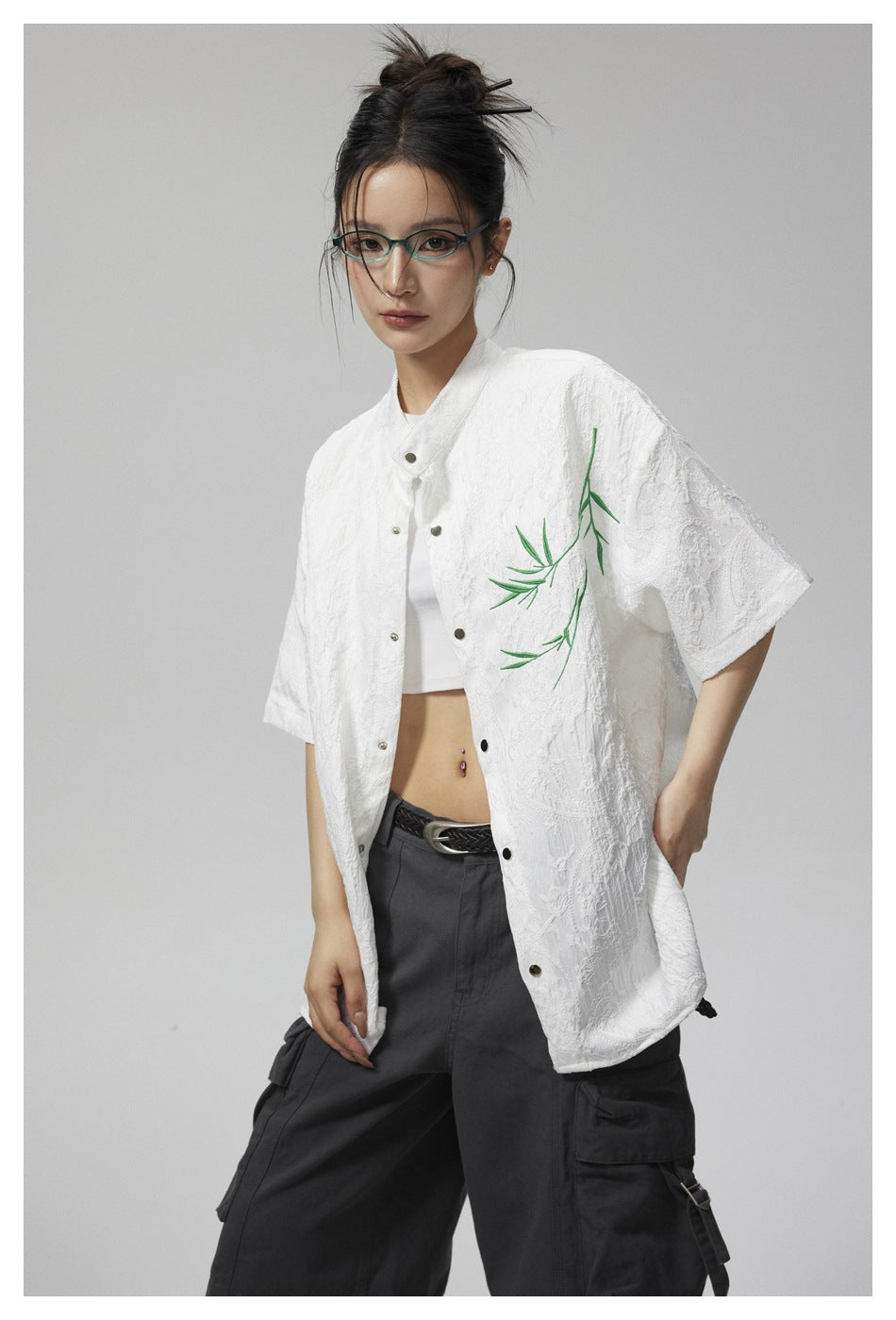 Model wearing a white textured short-sleeve shirt with green bamboo embroidery over a white crop top.