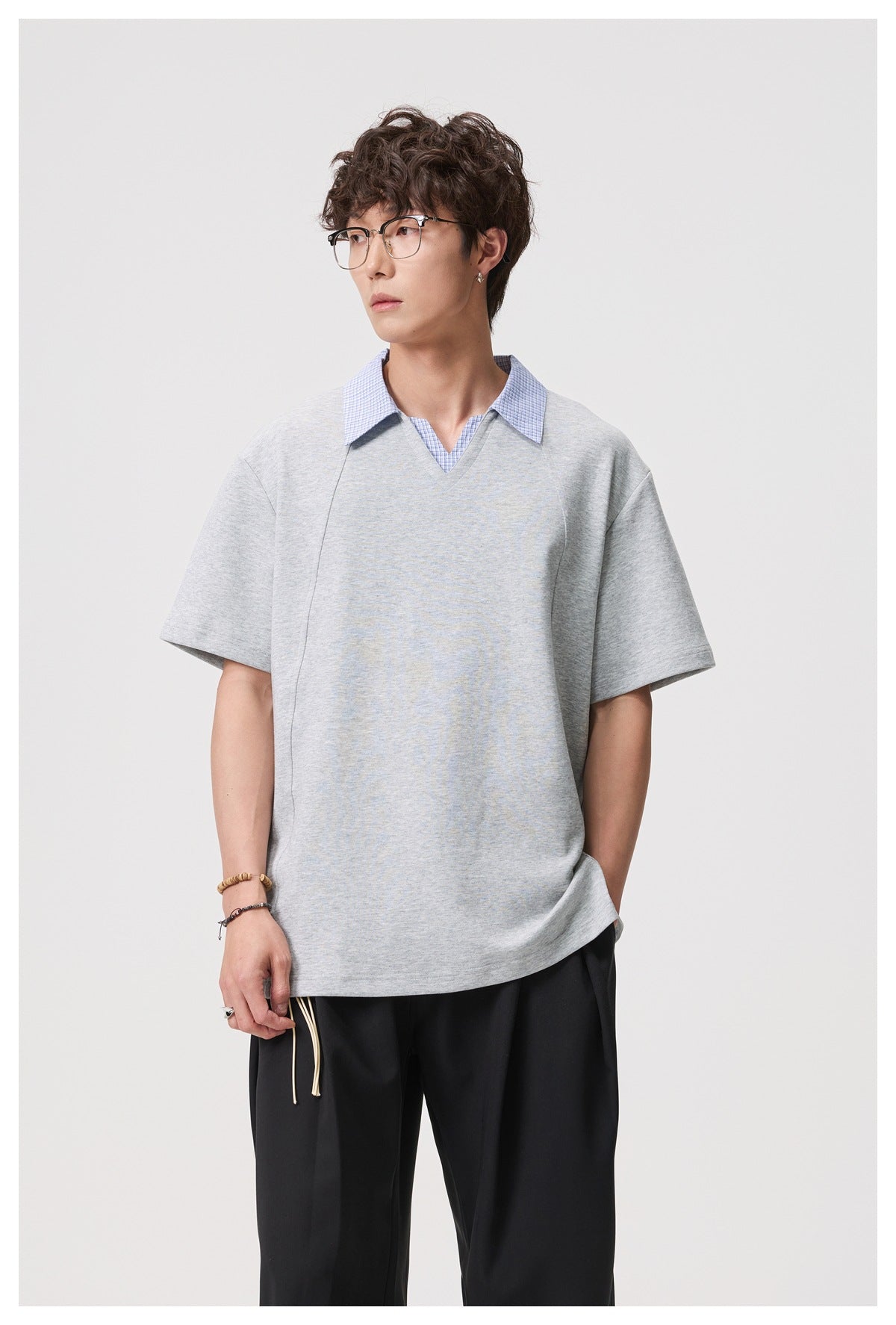Model wearing a light gray short-sleeve V-neck top with a blue checked collar and black trousers.